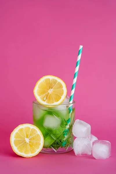 Ice cubes in glass with mojito drink and straw near lemons on pink — Stock Photo