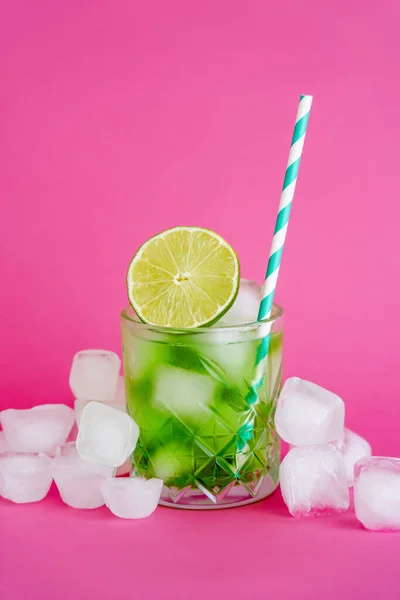 Ice cubes in faceted glass with mojito drink and sliced lime on pink — Photo de stock