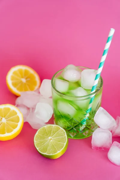 Ice cubes in glass with mojito drink and straw near citrus fruits on pink — Photo de stock