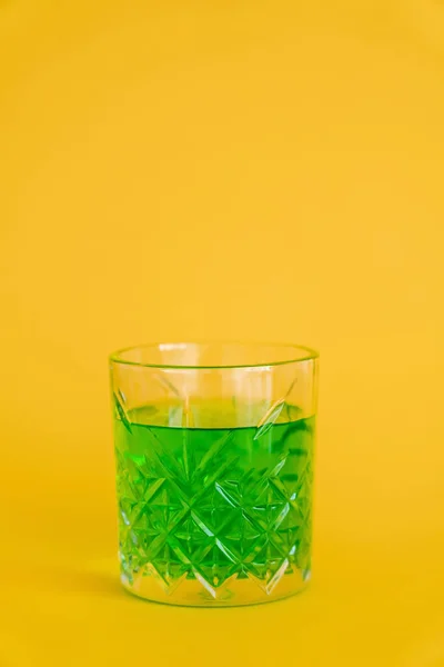 Faceted glass with green alcohol drink on yellow — Foto stock