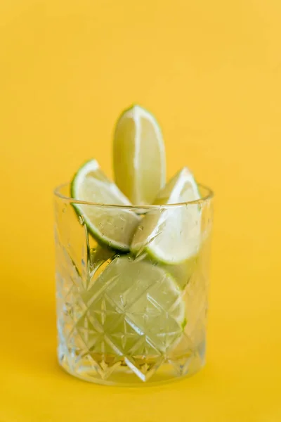 Cool faceted glass with sliced fresh limes on yellow — Stock Photo