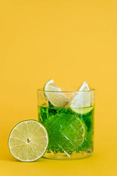 Limas fatiadas em vidro com bebida mojito espumante em amarelo — Fotografia de Stock