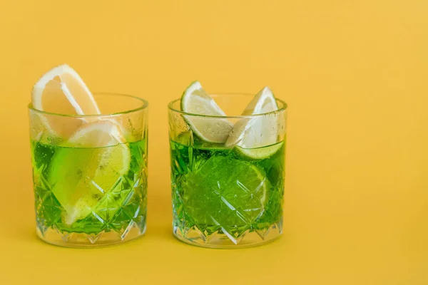 Sliced citrus fruits in glasses with sparkling mojito drink on yellow — Stock Photo