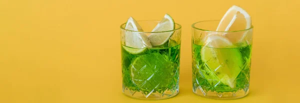 Sliced citrus fruits in glasses with sparkling mojito drink on yellow, banner — Stock Photo