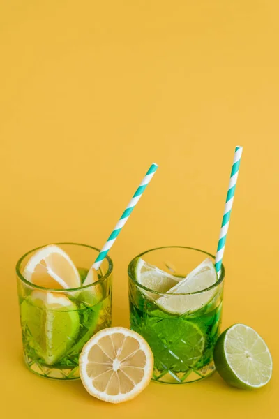 Sliced citrus fruits in glasses with sparkling mojito drink and straws on yellow - foto de stock