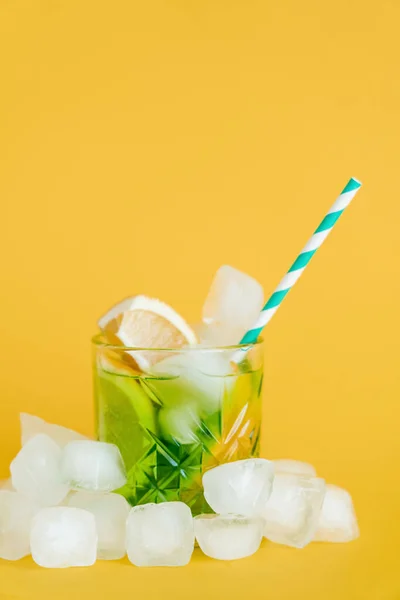 Ice cubes and sliced lemons in glass with mojito drink on yellow — Stock Photo