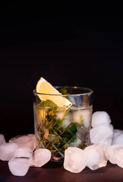 Verre à facettes cool avec mojito près de glaçons sur noir — Photo de stock