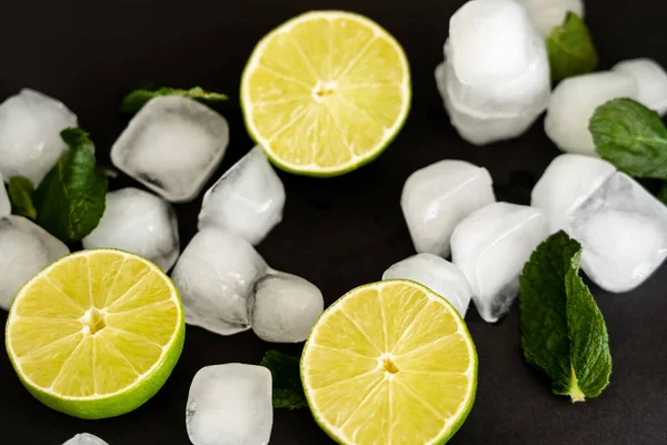 High angle view of melting ice cubes near sliced limes on black background — Photo de stock