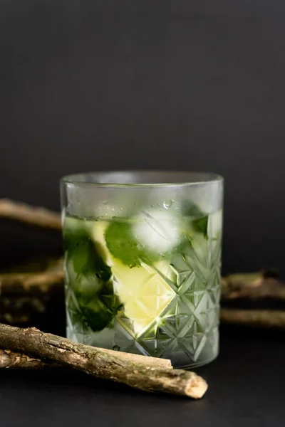 Faceted cold glass with melting ice cubes and sliced lime near wooden sticks on black — Photo de stock