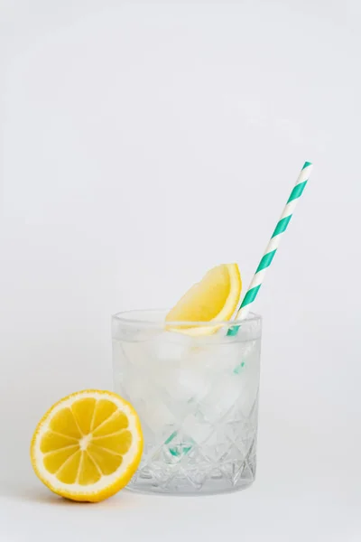 Faceted cold glass with ice cubes, paper straw and sliced lemons on white — Fotografia de Stock