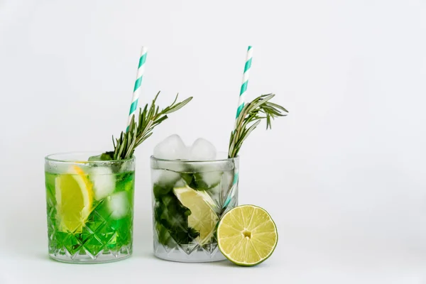 Cool faceted glasses with cocktails and ice cubes near citrus fruits on white — Fotografia de Stock