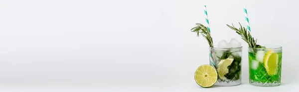 Kühle facettierte Gläser mit Cocktails und Eiswürfeln in der Nähe von Zitrusfrüchten auf weißem Banner — Stockfoto