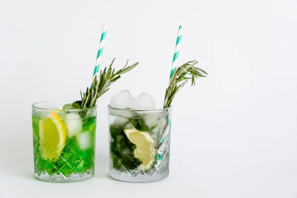 Faceted glasses with cocktails, ice cubes and citrus fruits on white — Stockfoto