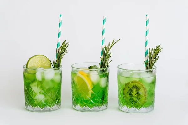 Грановані окуляри з зеленим коктейлем, кубиками льоду та фруктами на білому — стокове фото