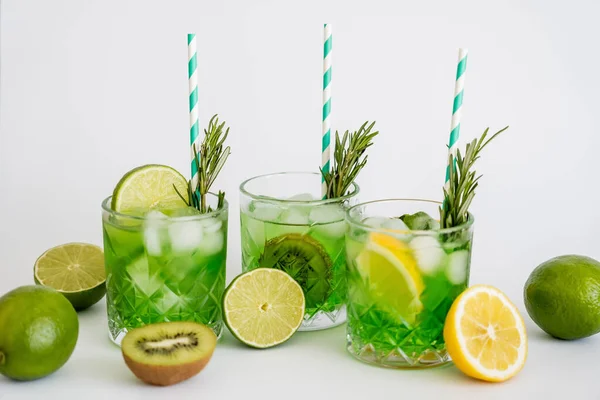 Bicchieri sfaccettati con cocktail verde freddo, cannucce e frutta su bianco — Foto stock