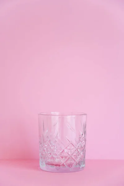 Empty and transparent faceted glass on pink background — Fotografia de Stock