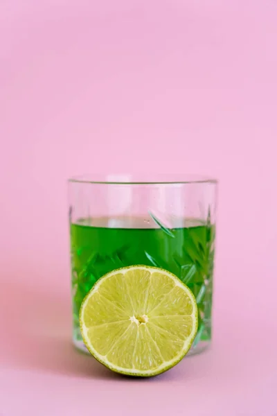 Limão fresco verde perto de bebida alcoólica em vidro em rosa — Fotografia de Stock