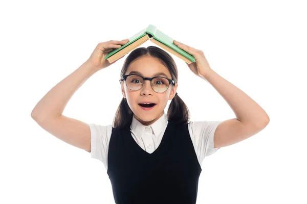 Positive schoolkid in eyeglasses holding book above head isolated on white — Stock Photo