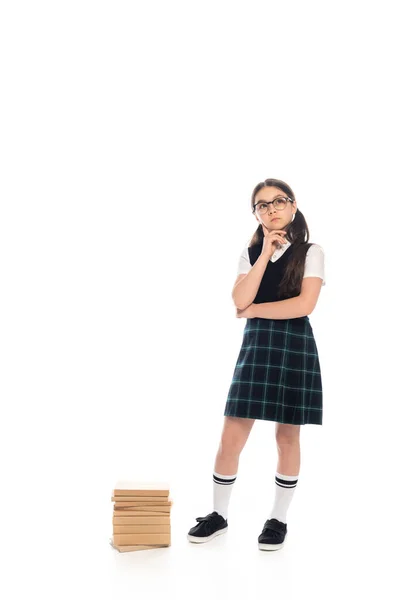 Pensive Schulkind in Rock und Brille steht neben Büchern auf weißem Hintergrund — Stockfoto