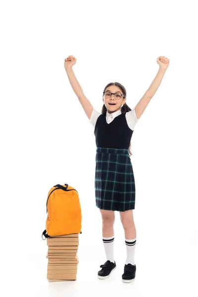 Aufgeregtes Schulkind mit Brille zeigt Ja-Geste neben Büchern und Rucksack auf weißem Hintergrund — Stockfoto