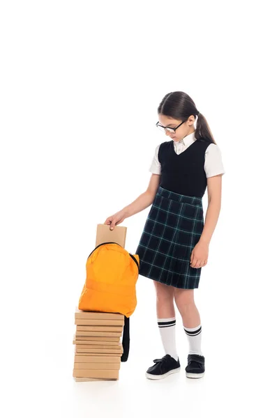 Longitud completa de la colegiala preadolescente poniendo libro en la mochila sobre fondo blanco - foto de stock