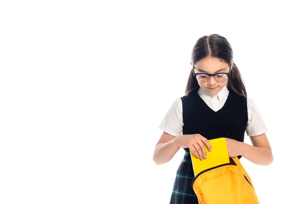 Preadolescente escolar en gafas poniendo libro en la mochila aislado en blanco - foto de stock