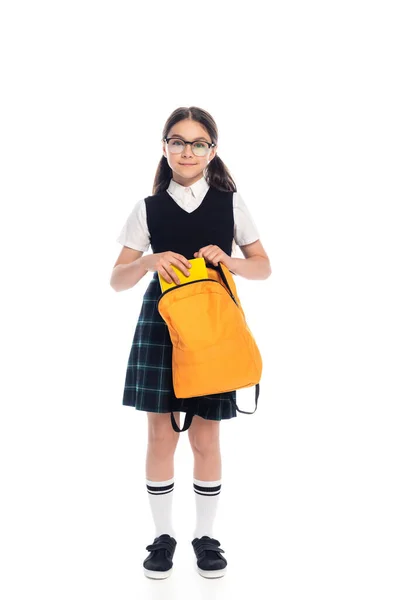 Full length of cheerful pupil putting book in backpack on white background — Stock Photo