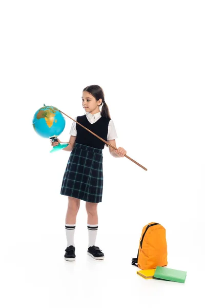 Preteen écolière tenant pointeur et globe près de livres et sac à dos sur fond blanc — Photo de stock