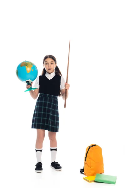 Shocked schoolgirl holding globe and pointer near backpack and books on white background — Stock Photo