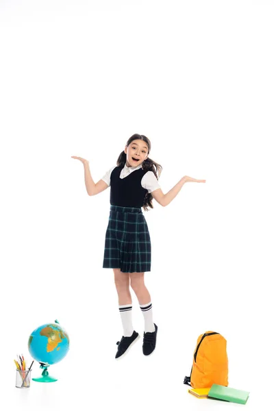 Позитивный школьник, указывая руками, прыгая рядом с земным шаром и книги на белом фоне — стоковое фото