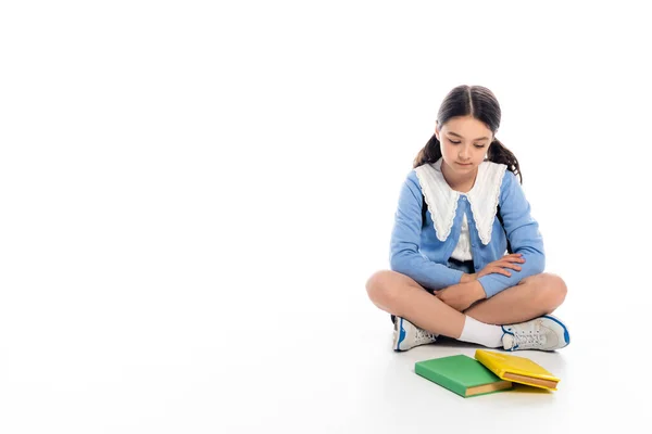 Schulkind schaut Bücher an, während es auf weißem Hintergrund sitzt — Stockfoto