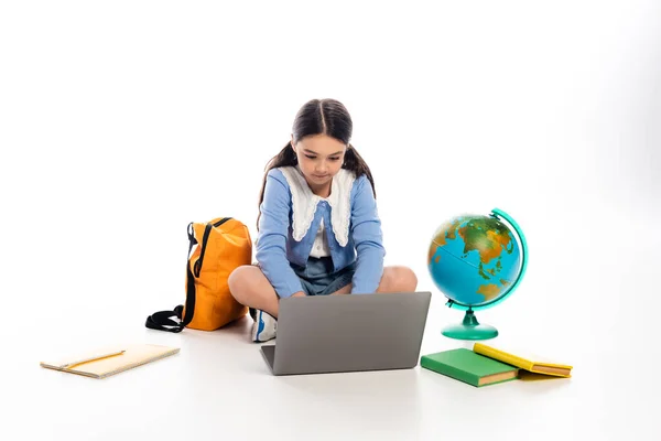 Schoolkid usando laptop perto de livros e globo no fundo branco — Fotografia de Stock
