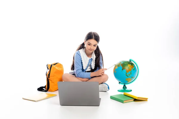 Niño de la escuela apuntando al guante cerca de la computadora portátil y libros sobre fondo blanco — Stock Photo