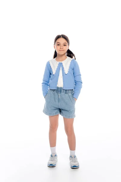 Full length of schoolgirl holding hands in pockets of denim shorts on white background — Stock Photo