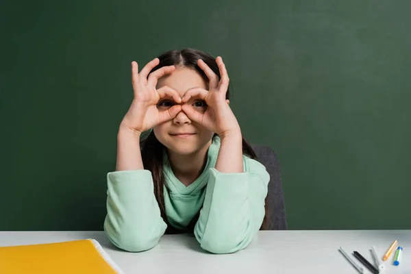 Preteen schoolkid gesturing near notebook and chalkboard at background — Stock Photo