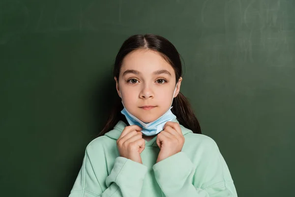 Estudante segurando máscara médica perto de quadro no fundo — Fotografia de Stock