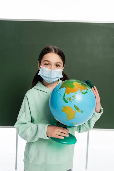 Pupil in medical mask holding globe near chalkboard isolated on white — Stock Photo