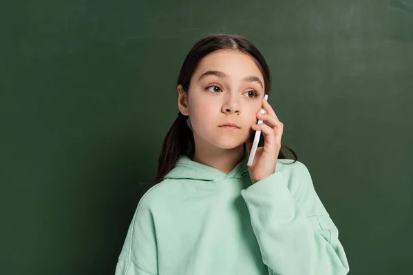 Aluno pré-adolescente falando no celular perto de quadro no fundo — Fotografia de Stock