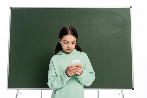 Preteen schoolkid using mobile phone near chalkboard isolated on white — Stock Photo