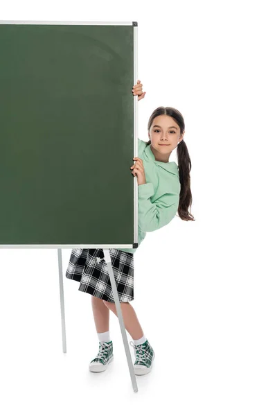 Comprimento total de colegial sorrindo em pé perto de quadro-negro no fundo branco — Fotografia de Stock