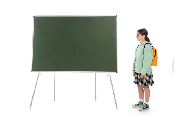 Vue latérale de l'écolier avec sac à dos debout près du tableau noir sur fond blanc — Photo de stock