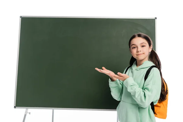 Smiling pupil with backpack pointing at chalkboard isolated on white — Stock Photo