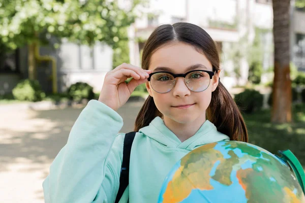 Portrait of schoolgirl holding eyeglasses and globe outdoors — Stock Photo