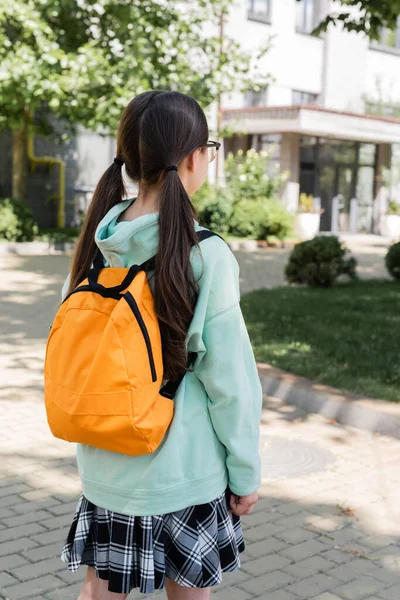Back view of brunette schoolgirl with backpack standing on urban street — Stock Photo