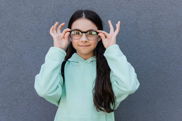 Smiling preteen pupil holding eyeglasses near building outdoors — Stock Photo