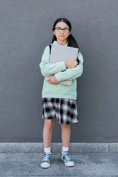 Pupil in eyeglasses holding laptop near building outdoors — Stock Photo