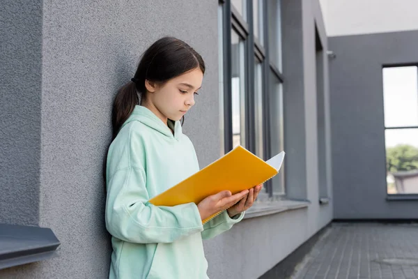 Preteen Schülerin schaut auf Notizbuch in der Nähe Gebäude im Freien — Stockfoto