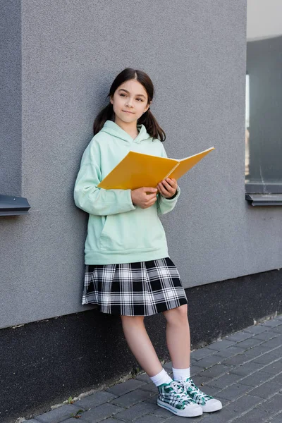 Школьник в юбке держит ноутбук рядом со зданием на городской улице — стоковое фото