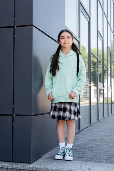 Schoolgirl with backpack standing near building on urban street — Stock Photo