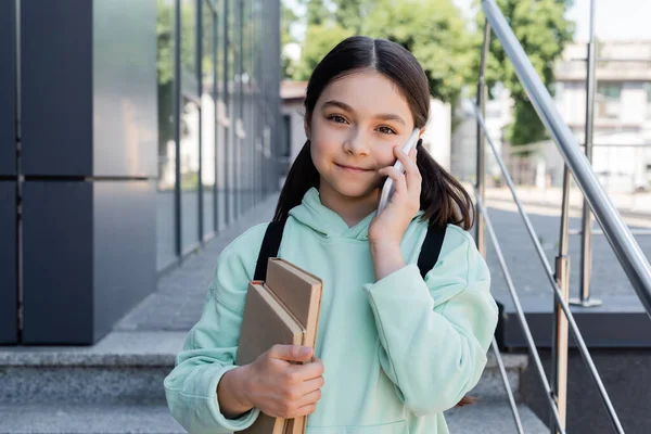 Ritratto di allievo con libri che parlano al cellulare su strada urbana — Foto stock